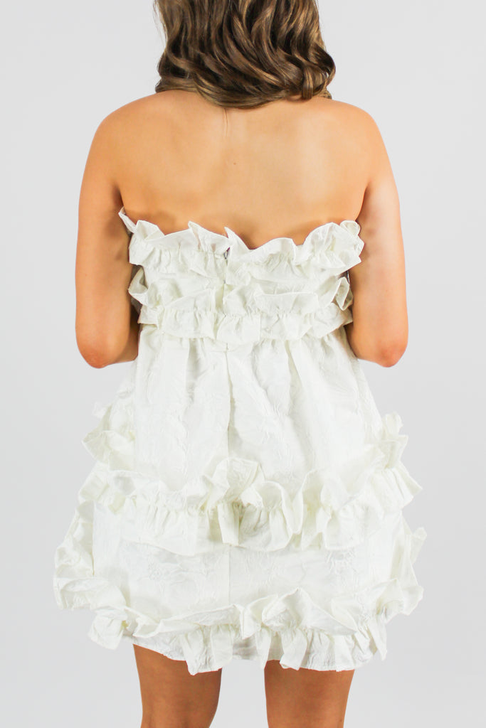 back photo of an off white mini dress with ruffle detail and a floral texture pattern