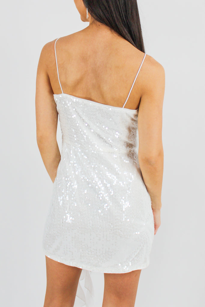 back photo of white sequin mini dress with spaghetti straps and a ruffle flower detail