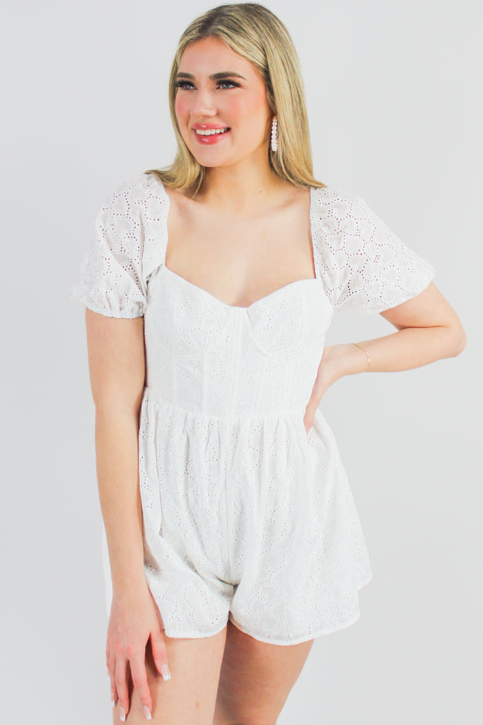 white eyelet romper with heart details in the lace, puff sleeves, and a corset top.
