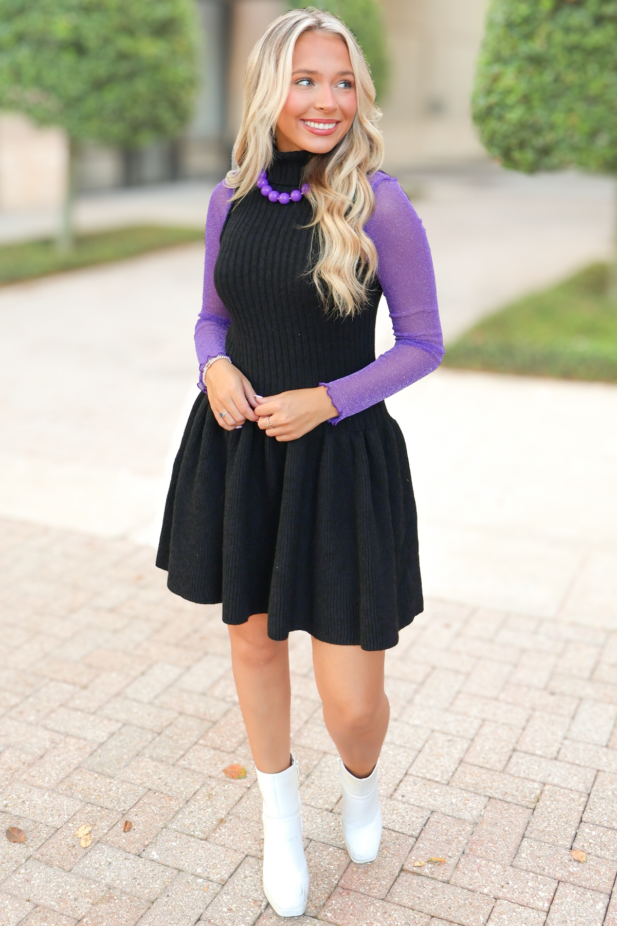 Sleeveless ribbed knit sweater dress layered over a purple shimmer mock neck mesh top