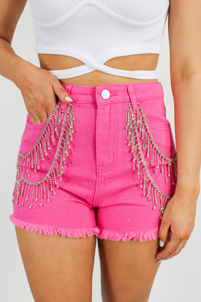 hot pink denim shorts with rhinestone fringe detail along the front.