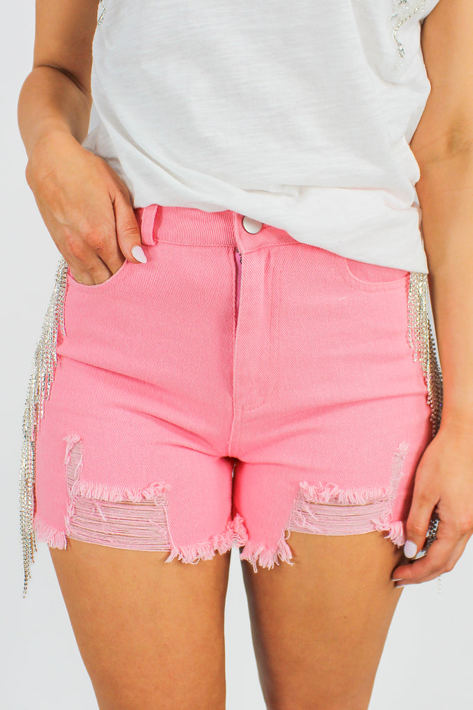 pink denim shorts with distressed hem and rhinestone fringe on the sides
