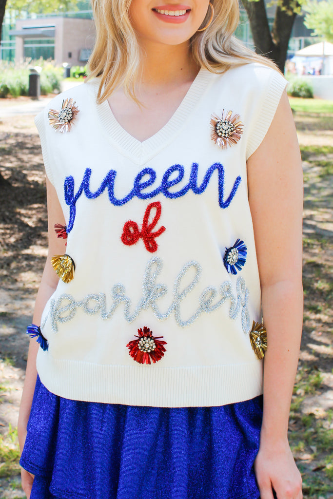 Close up front view of Our Sparklers Sweater Vest by Queen of Sparkles comes in ivory with red, blue and silver sparkle tinsel trim creating cursive writing on the front under the vneck neck. this sleeveless sweater has red, blue and gold tinsel, embellished decals all over.