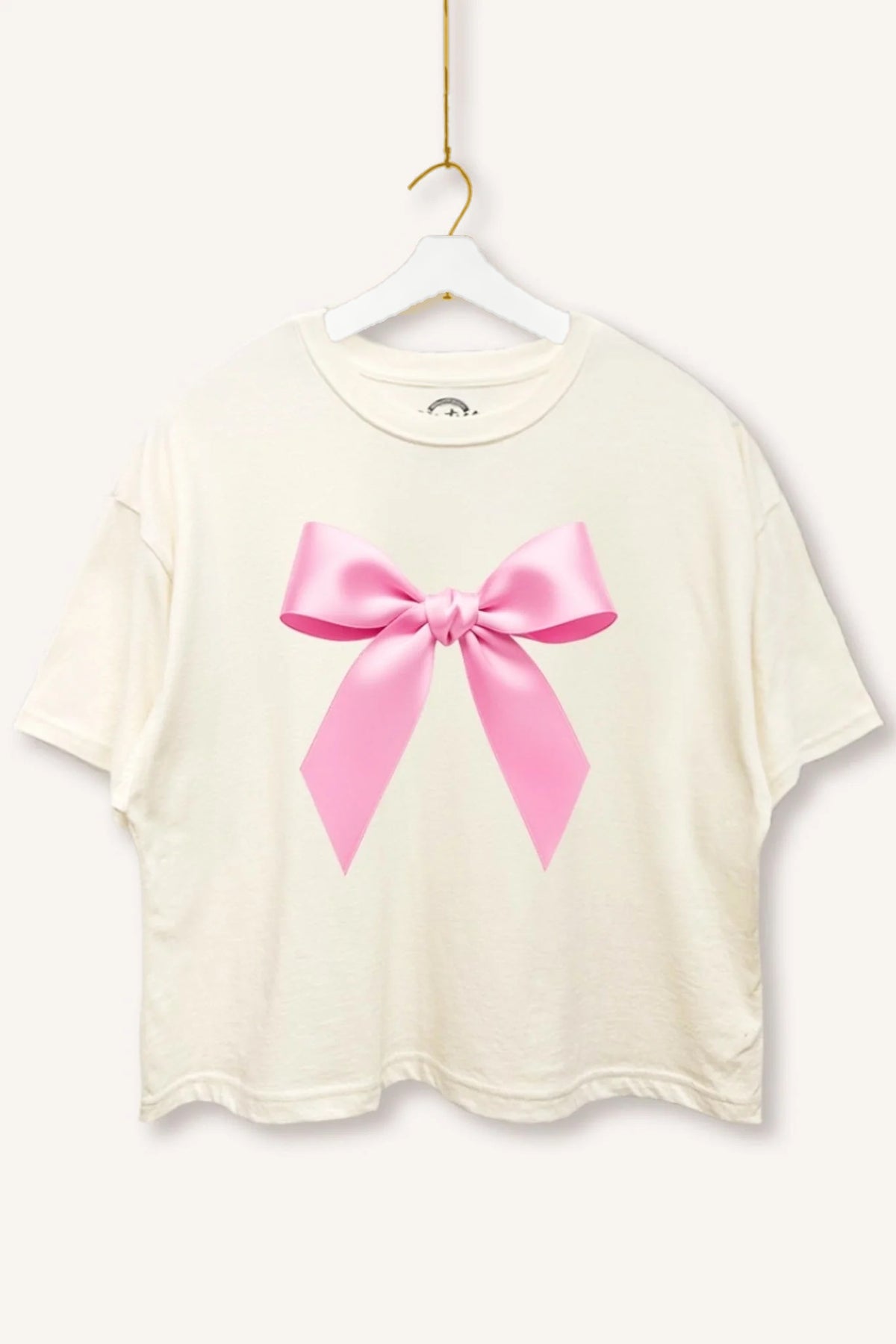 Charming Cues Ribbon Boxy Crop Tee in Cream with pink bow graphic on a white hanger