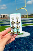 Confetti Fleur De Lis Earrings by Taylor Shaye in Black/Gold on card at a football field