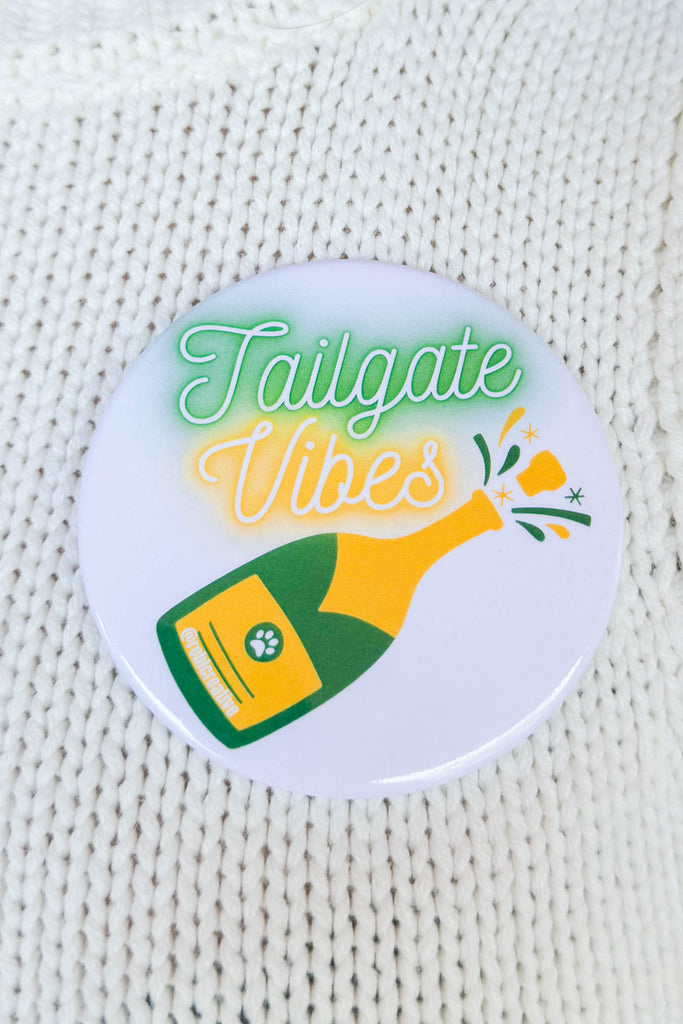 button with neon cursive writing of "tailgate vibes" with champagne bottle popping in yellow and green